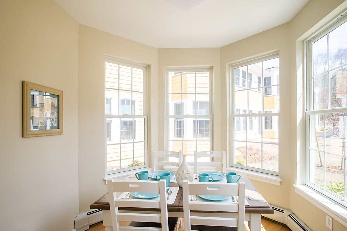 A brightly lit dining area with a neatly set table in front of large windows.
