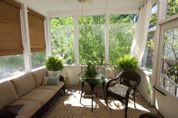 A cozy sunroom filled with natural light, featuring comfortable seating and lush greenery.