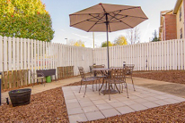 A cozy outdoor patio with a table, chairs, and an umbrella in a fenced backyard.