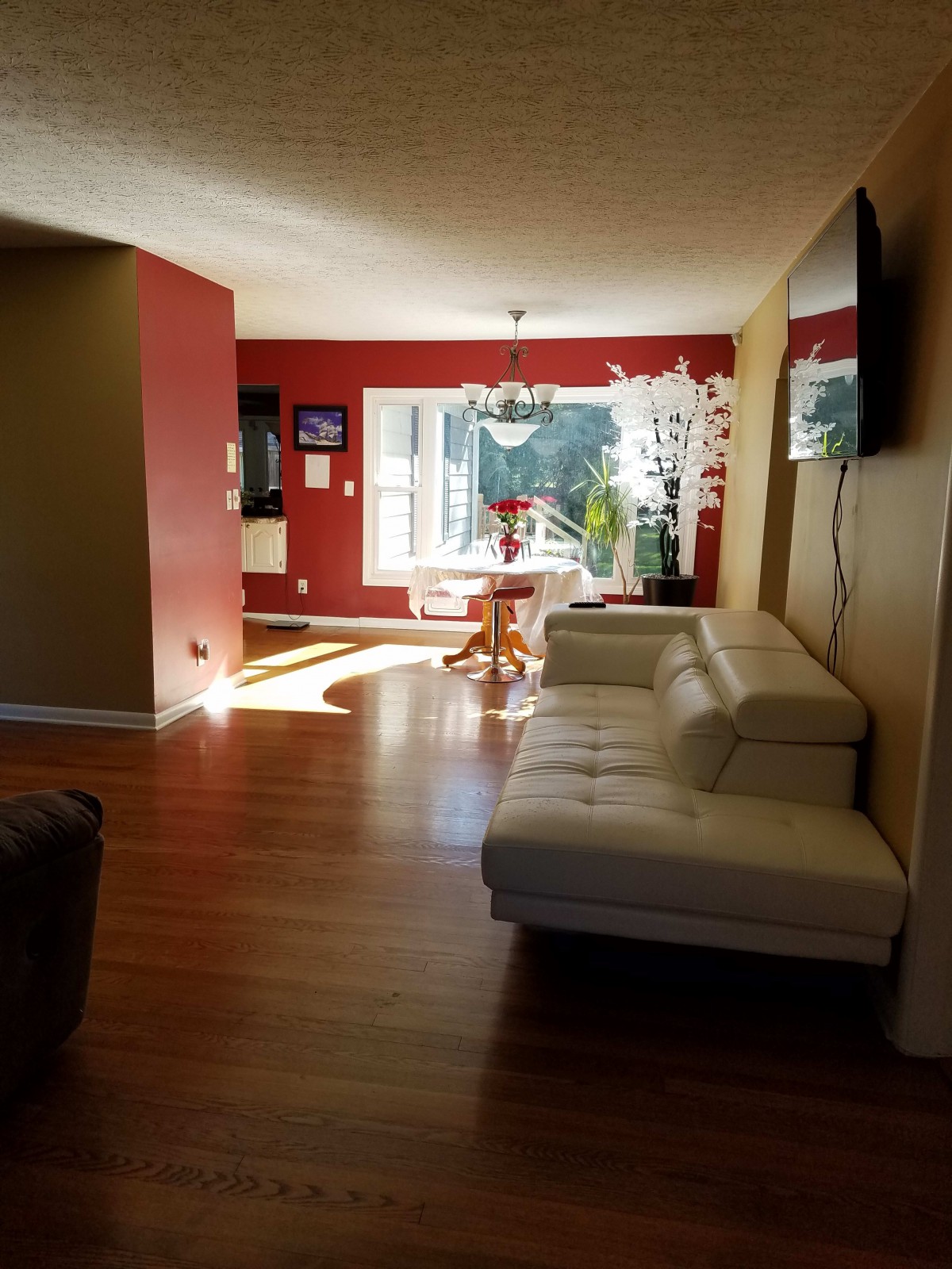 A modern living room with a white couch, dining area, and large windows allowing natural light.