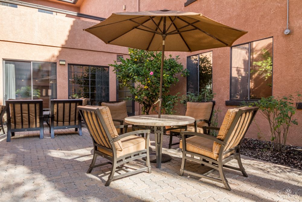 A cozy patio setup with a table, chairs, and an umbrella in a sunlit courtyard.