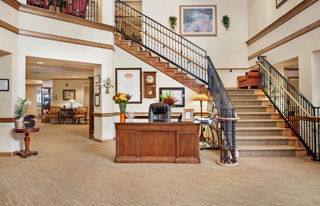 A warm and welcoming reception area featuring a wooden desk, staircase, and elegant decor.