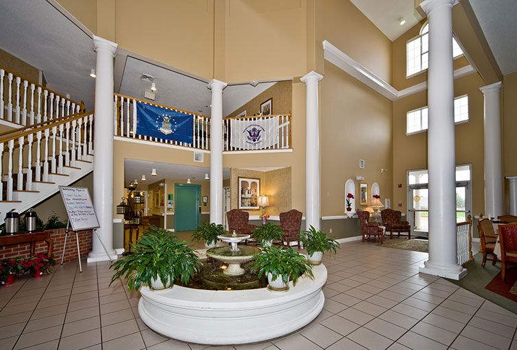 A spacious lobby area featuring a central fountain, surrounded by plants and seating, with flags hanging above and tall columns accentuating the architectural design.