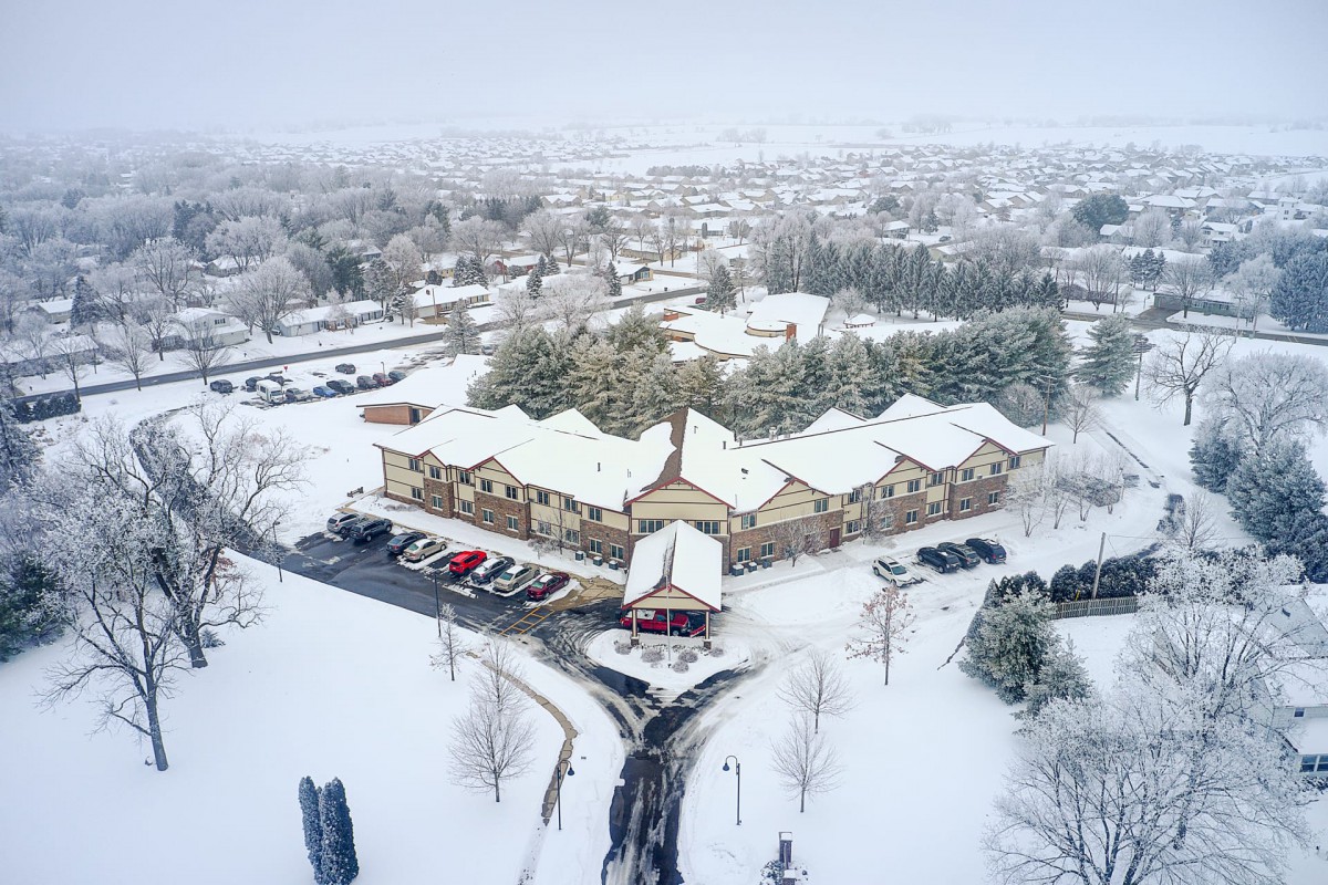 Aerial view of a snowy neighborhood with houses and trees blanketed in white on an overcast day.