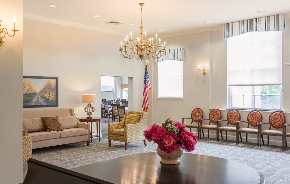 A well-furnished living room with a chandelier, comfortable seating, and a vase of flowers on the table.