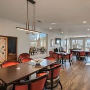 A modern dining area with elegant wooden tables and red cushioned chairs, featuring stylish lighting fixtures.
