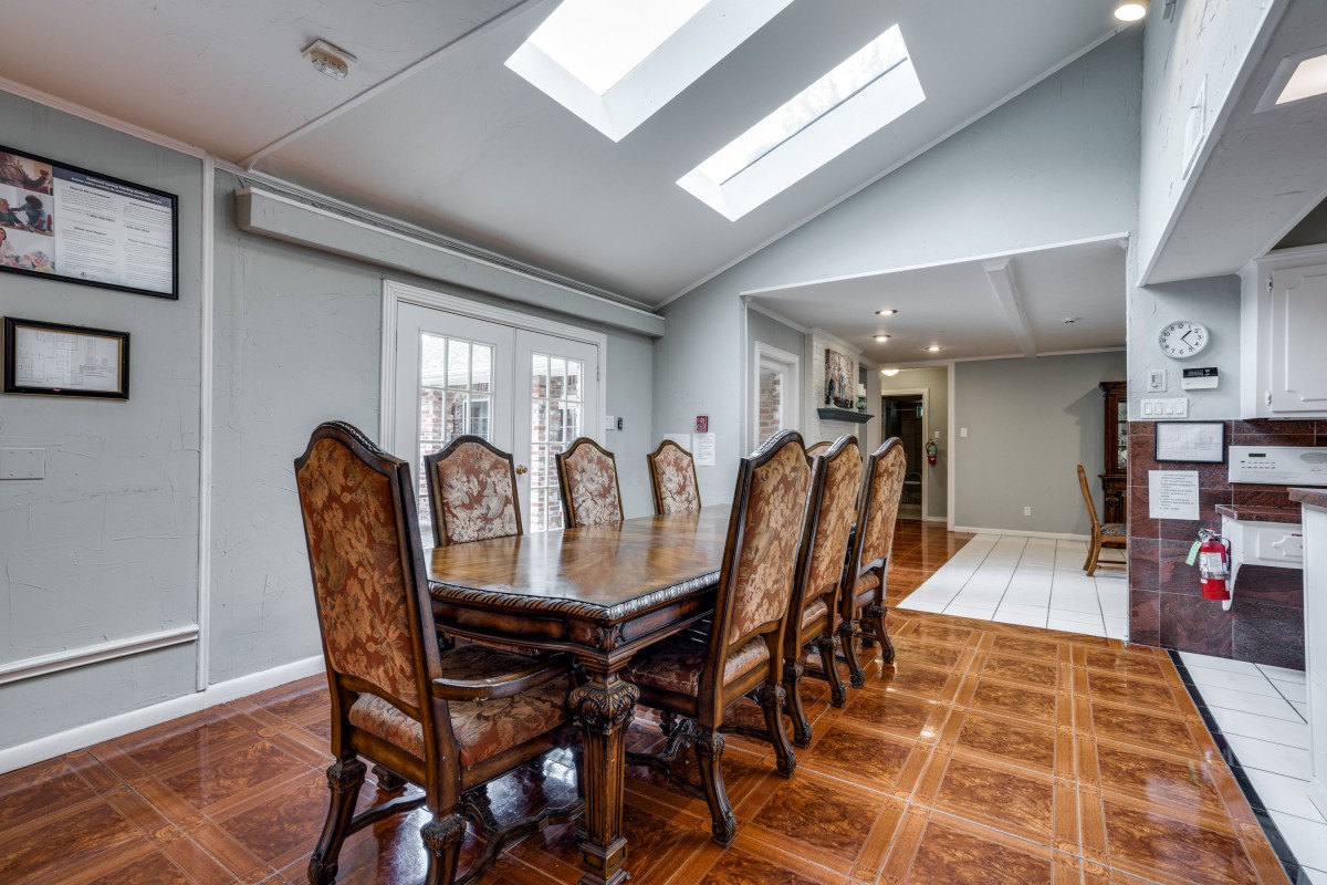 A spacious dining room featuring a long wooden table with ornate chairs, illuminated by natural light from skylights.