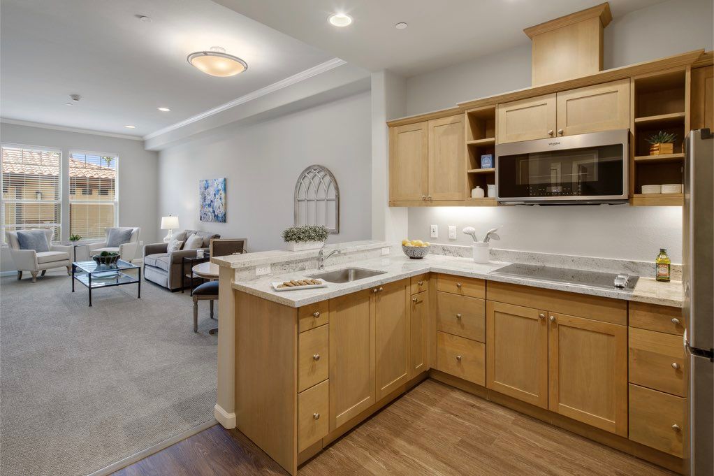 A modern kitchen with wooden cabinets opens into a living room, showcasing an open floor plan in an apartment interior.