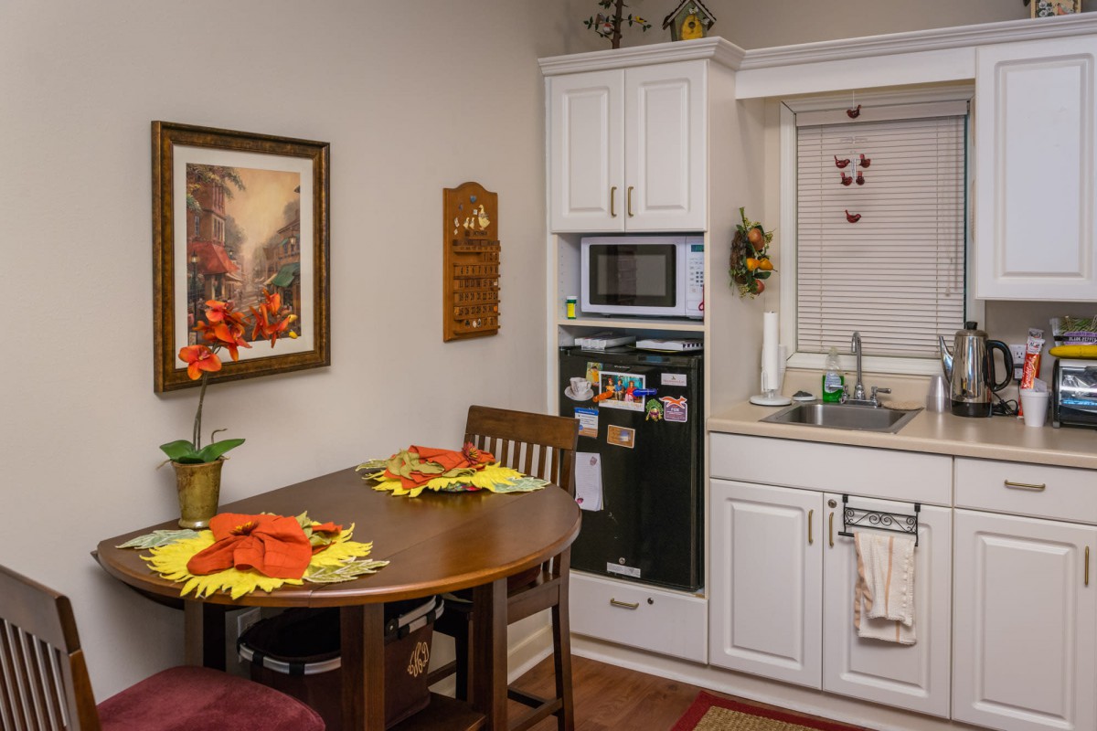 A cozy kitchen with a small dining table set for two, adorned with decorative flowers and a microwave nearby.