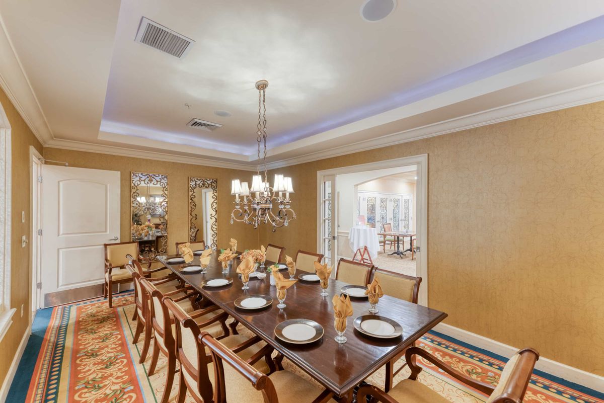 A spacious and elegantly decorated dining room featuring a long table set for a meal, complemented by a chandelier overhead.