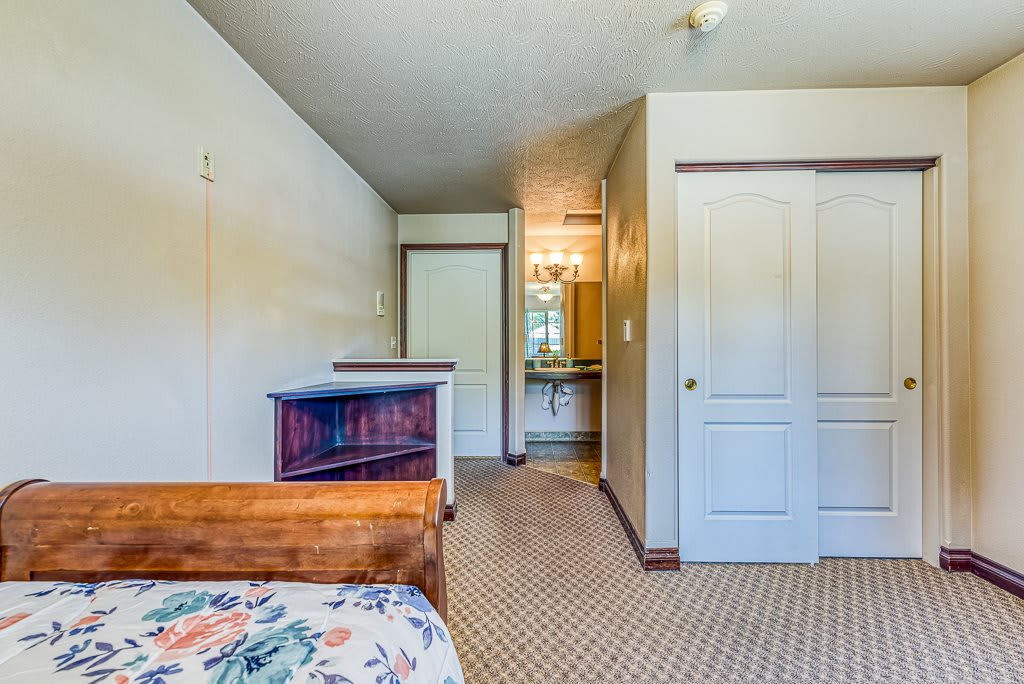 A cozy bedroom with a wooden bed, carpeted floor, and an adjoining bathroom area.