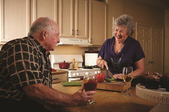 An elderly couple enjoying each other's company while preparing a meal in the kitchen.