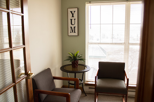 A cozy waiting area featuring two chairs, a small table with a plant, and natural light streaming through the window.