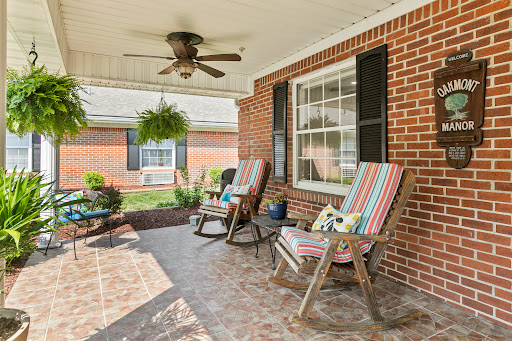 A cozy porch featuring colorful rocking chairs, a ceiling fan, and potted plants, perfect for enjoying a sunny day.