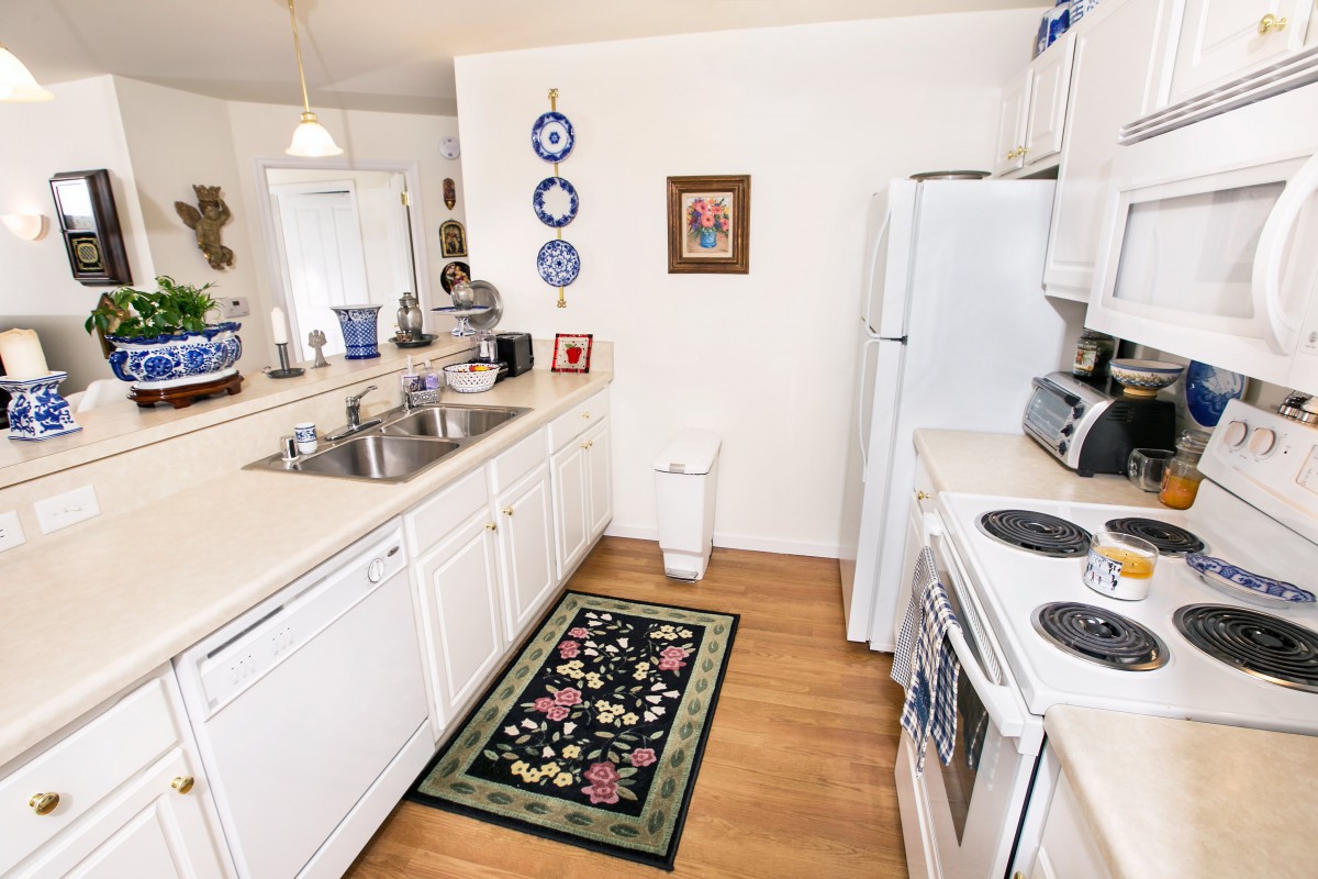 A bright kitchen with white cabinets, decorated plates, and a colorful rug on a wooden floor.