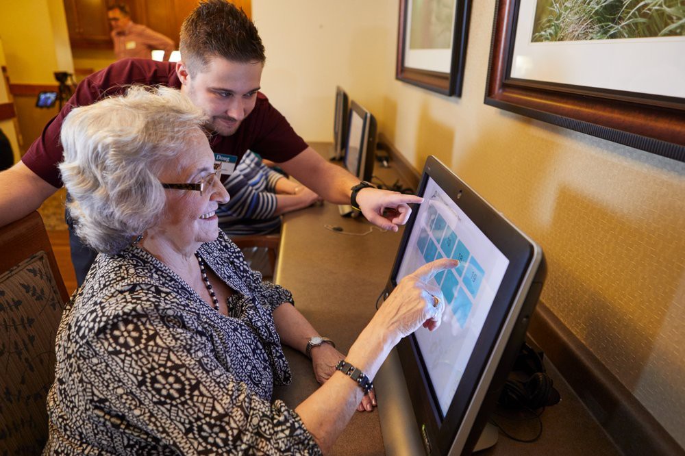 An elderly woman learns to use a computer with the assistance of a younger person.