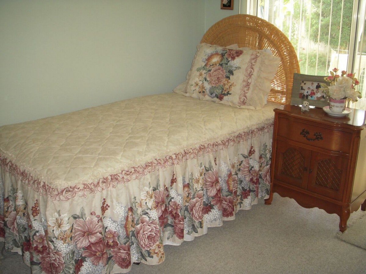 A cozy bedroom with a single bed featuring floral bedding and a wooden headboard, accompanied by a wooden nightstand.