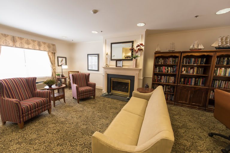 A cozy living room featuring a sofa, armchairs, fireplace, and bookshelf.
