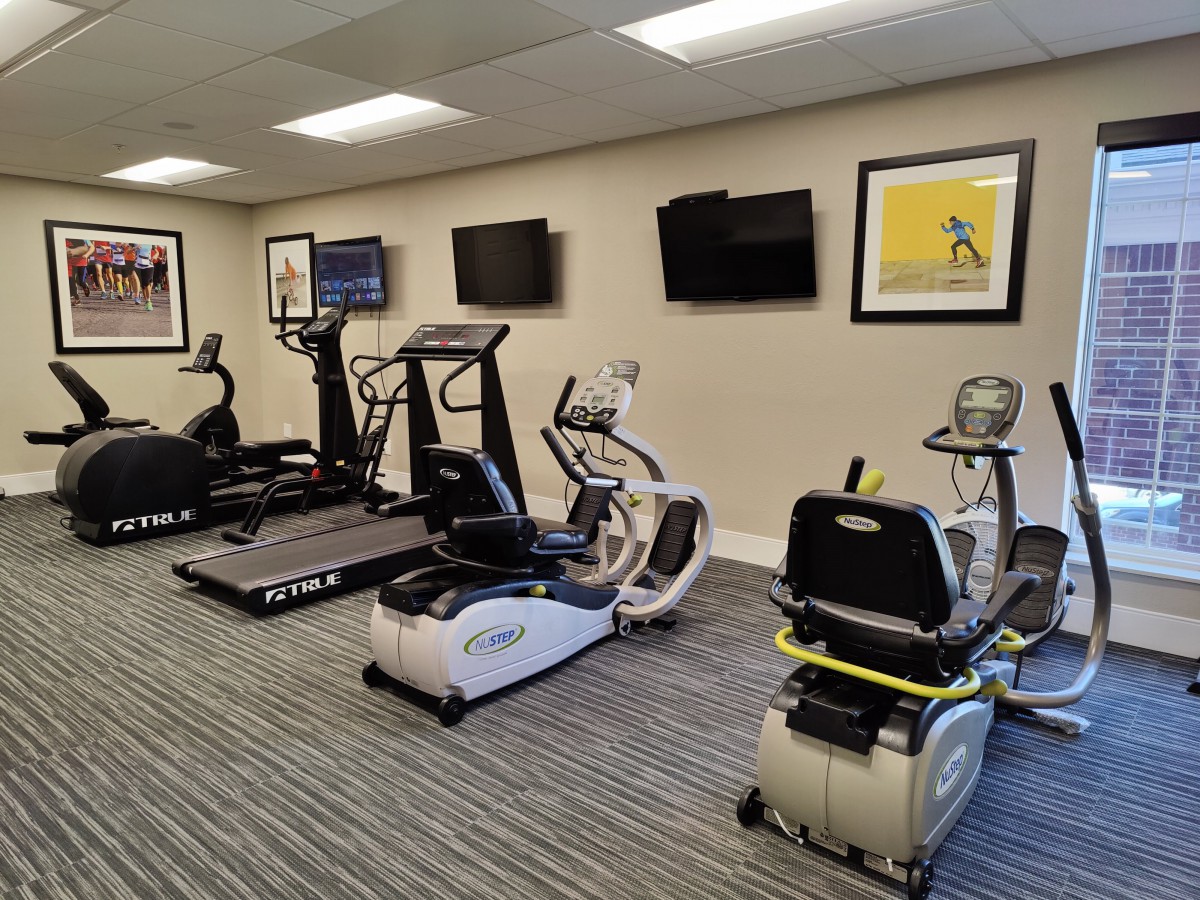 A well-equipped gym with various exercise machines and televisions on the wall.