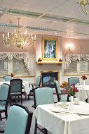 An elegant dining room featuring a chandelier and a fireplace with neatly arranged tables and chairs.