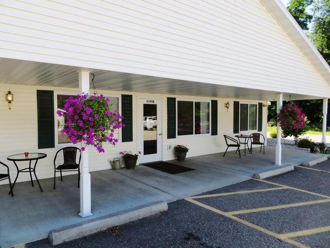The front entrance of a building with a covered porch, chairs, and hanging flower pots.