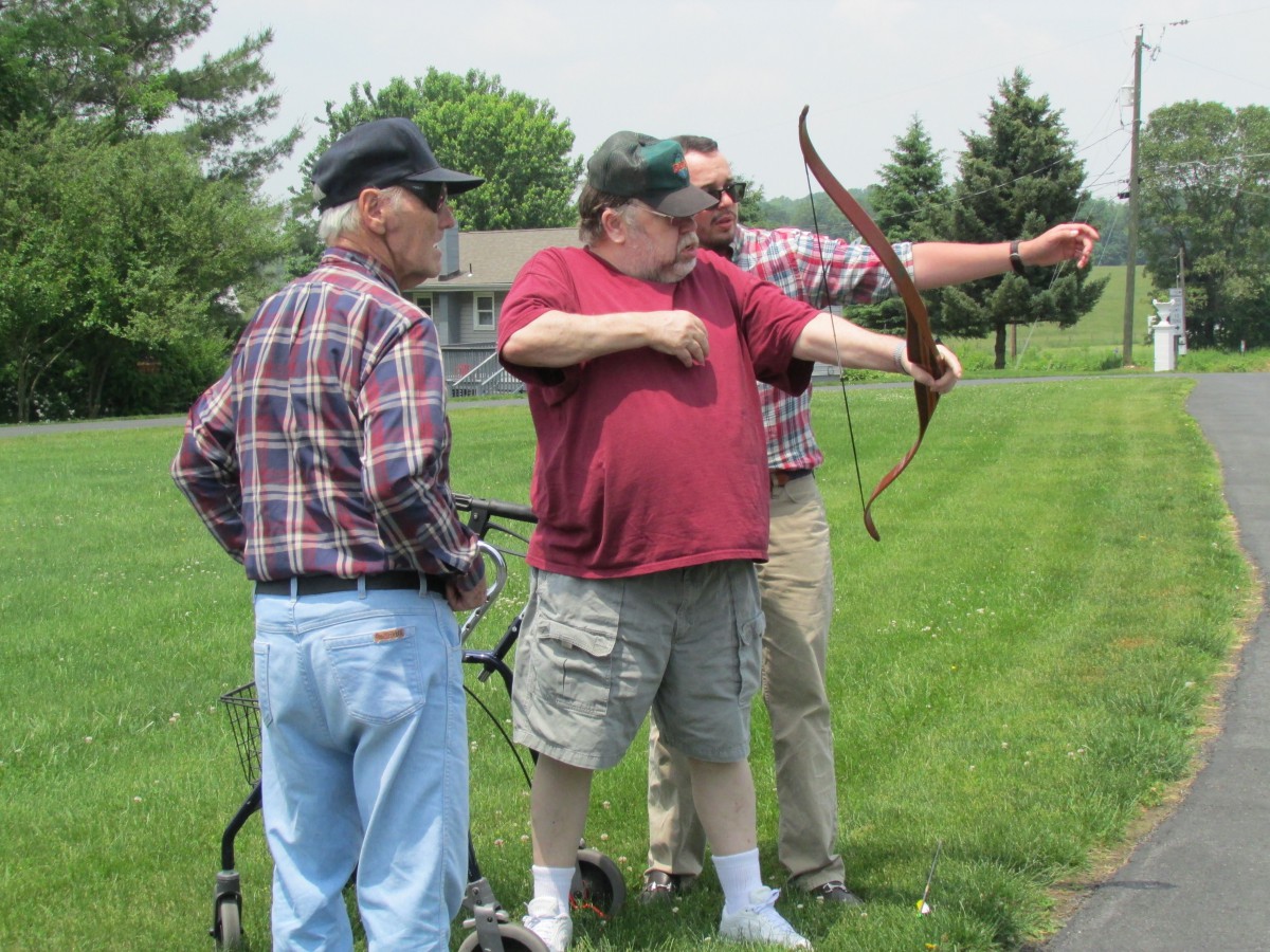 Three men practicing archery together outdoors on a grassy field.