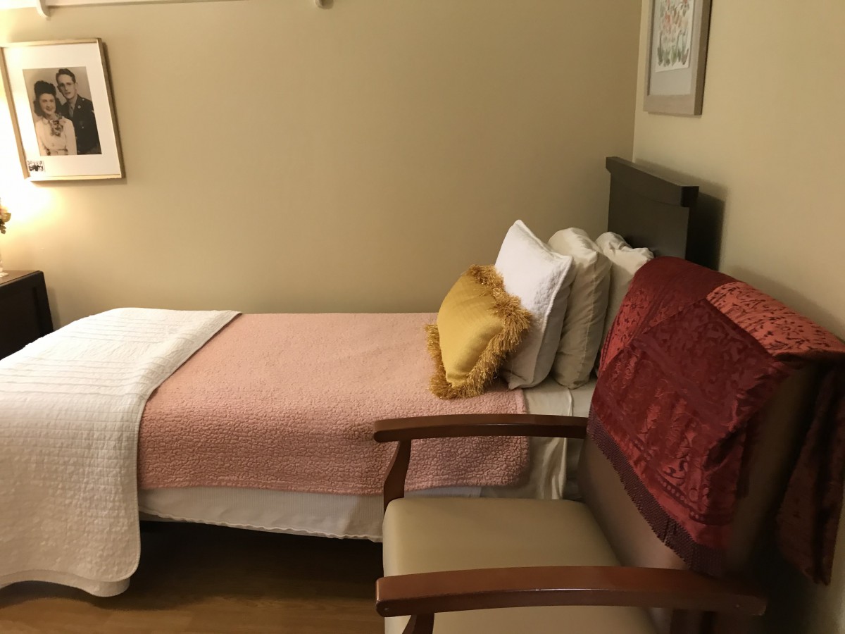 A cozy bedroom featuring a single bed with pillows and a blanket, accompanied by a comfortable chair.