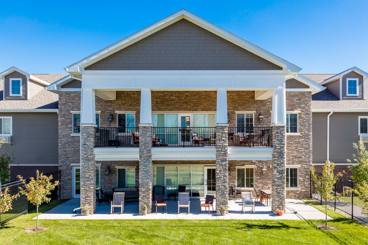 A two-story residential building with balconies and a patio area on a sunny day.