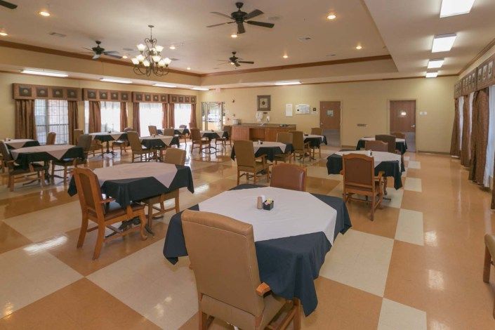 A spacious and well-lit dining area with neatly arranged tables and chairs, featuring ceiling fans and decorative lighting.