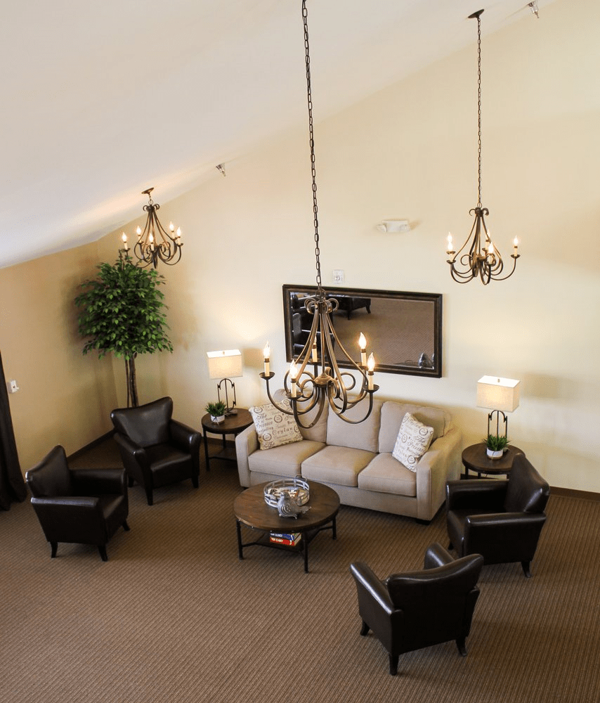 A stylish living room features a cozy sofa, elegant chandeliers, and a tasteful arrangement of chairs around a central coffee table.