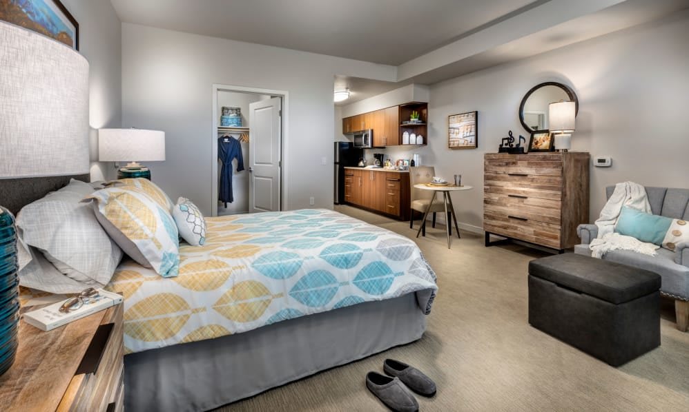 A modern and cozy bedroom with a bed, dresser, and small kitchenette.