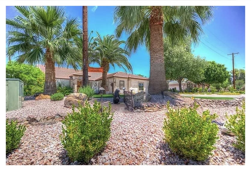 A charming house surrounded by palm trees and desert-style landscaping under a clear blue sky.
