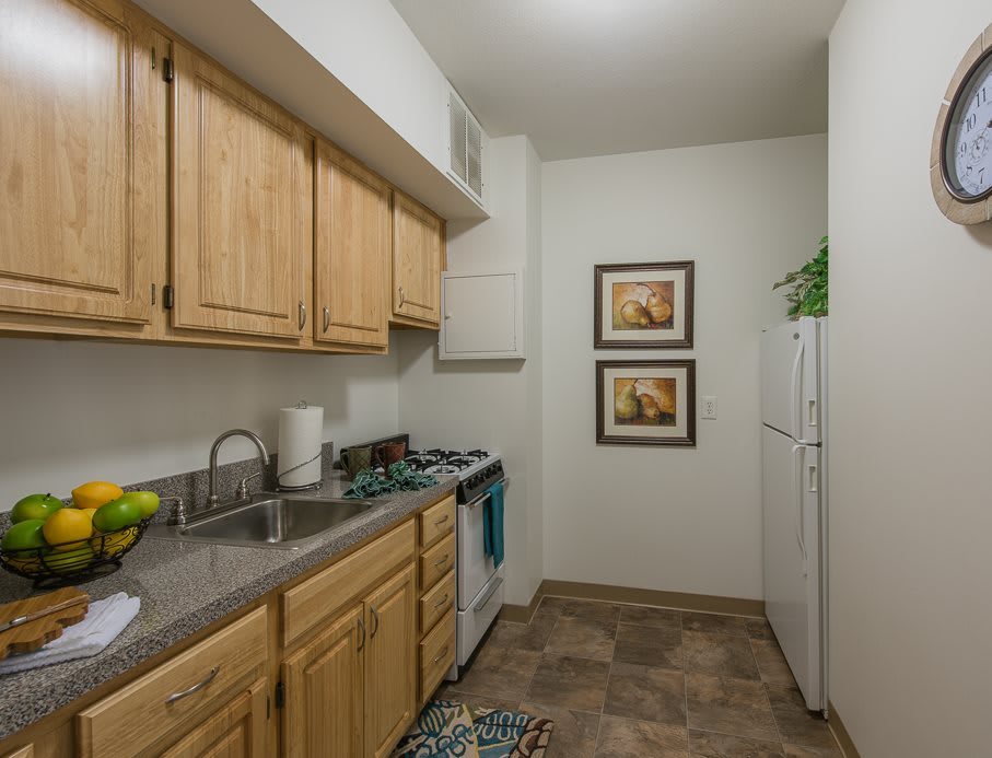 A compact kitchen with wooden cabinets, a stove, and decorative wall art.