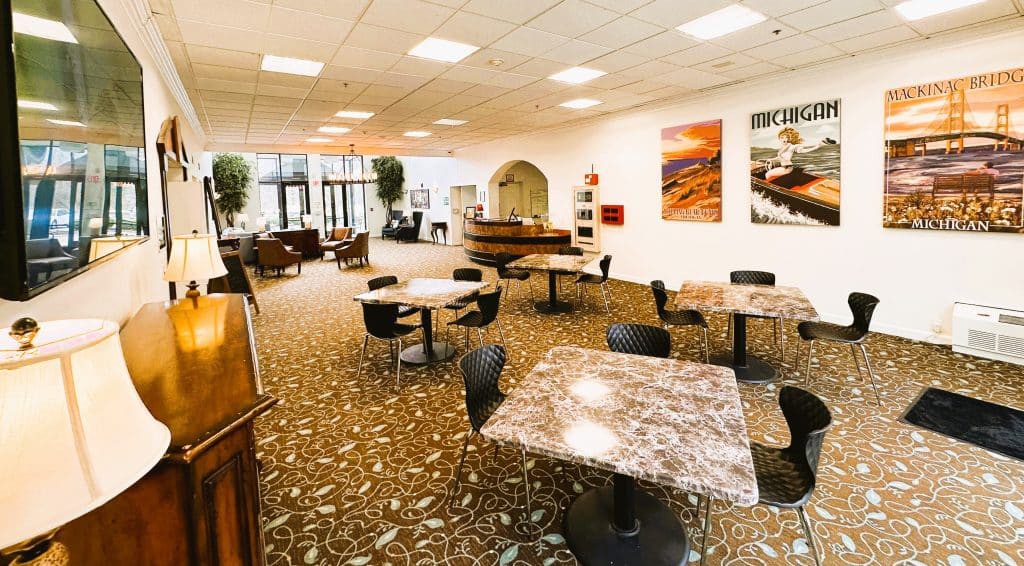 A modern indoor cafeteria with marble tables and black chairs, featuring artwork on the walls and a carpeted floor.