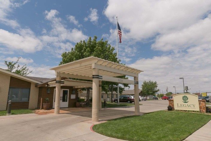 A building entrance with a canopy and an American flag waving in the background under a cloudy sky.
