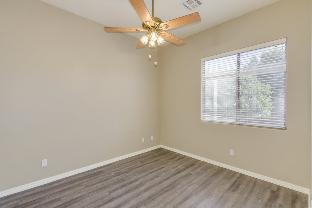An empty room with a ceiling fan and wooden flooring.