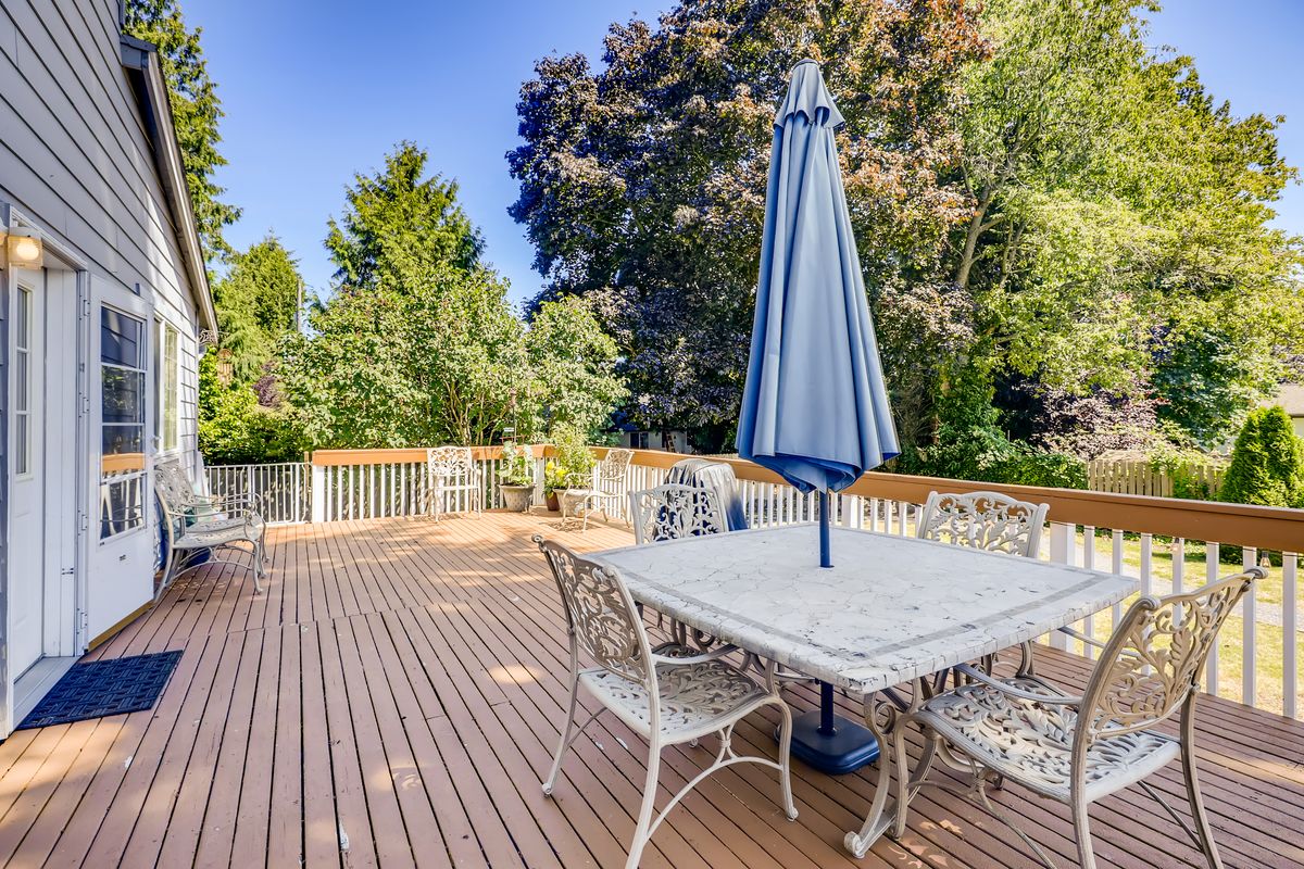 A spacious outdoor deck with a table, chairs, and an umbrella, surrounded by lush trees.