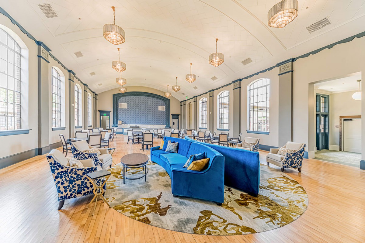 A spacious and modern lounge area featuring a blue couch, large windows, and contemporary lighting.