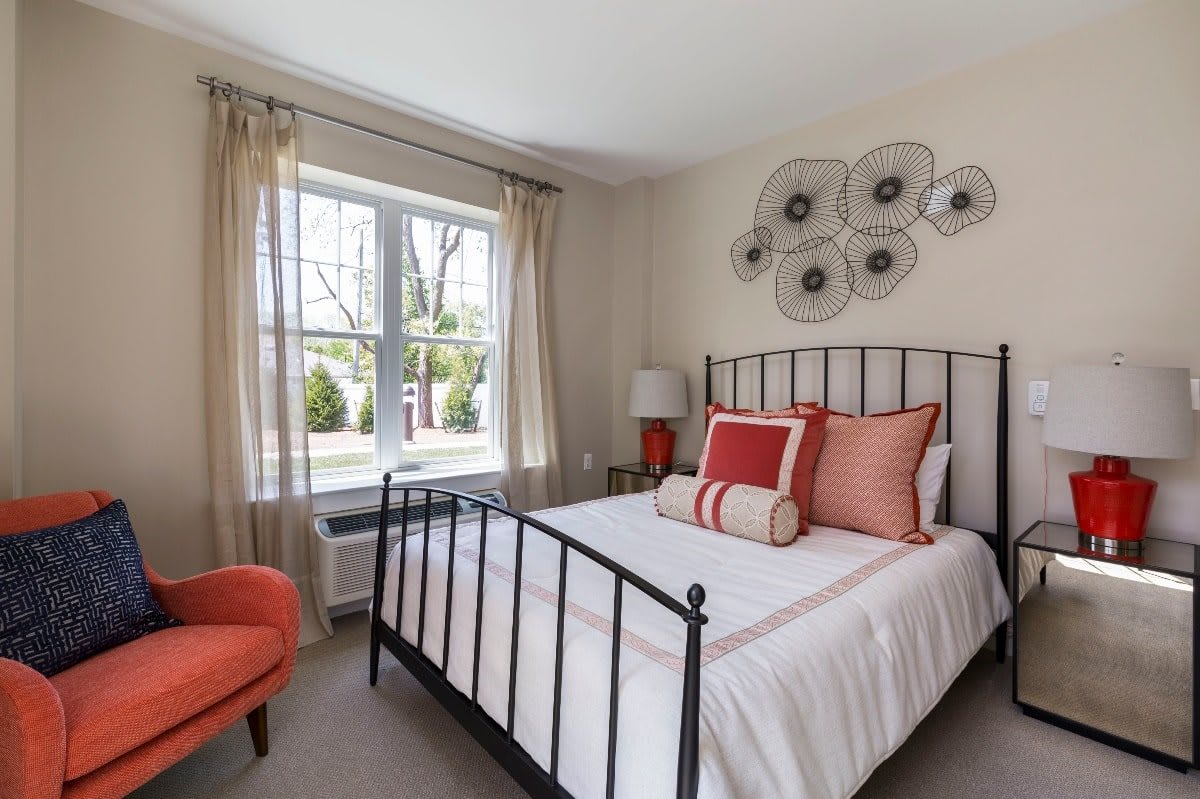A modern bedroom featuring a metal-frame bed with decorative pillows and natural light streaming through a large window.