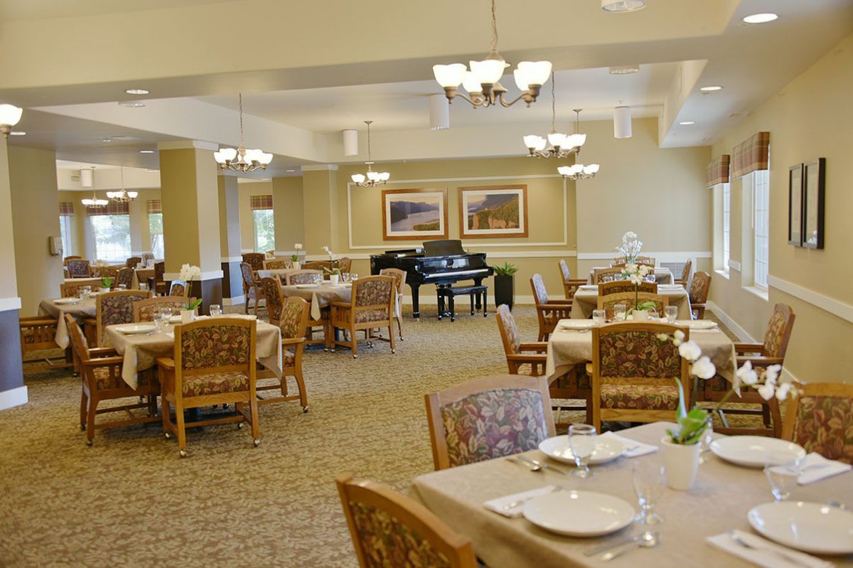 An empty dining room with neatly arranged tables and a grand piano.