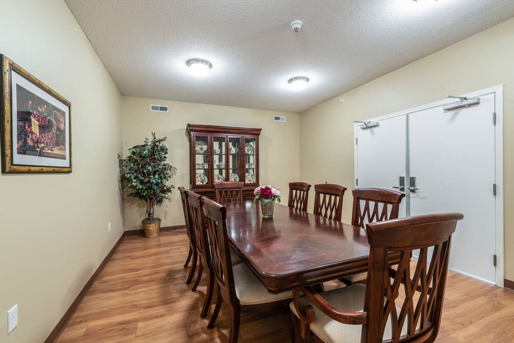 A dining room with a wooden table and chairs, featuring a cabinet and indoor plant.