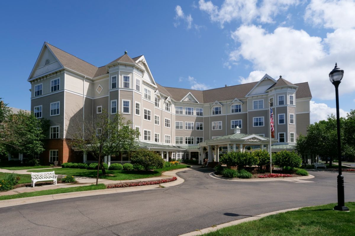 A large, multi-story hotel building with a landscaped entrance and driveway under a bright blue sky.