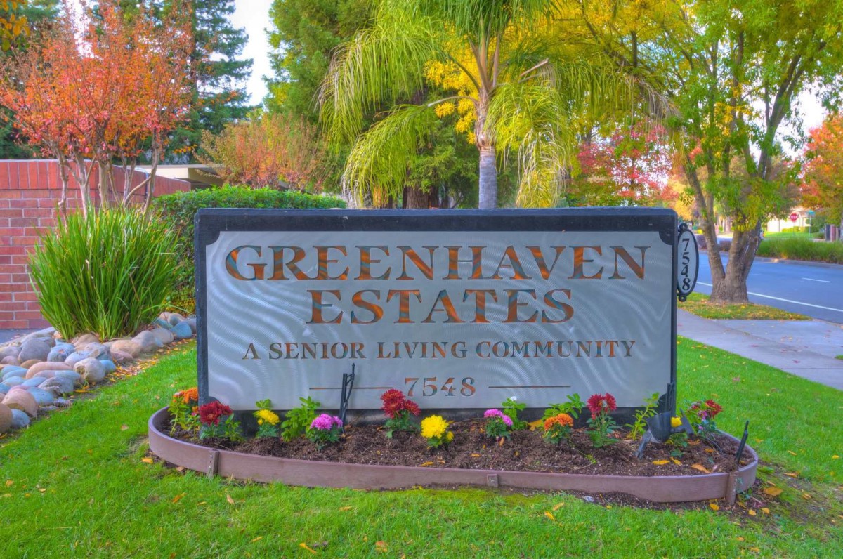 Entrance sign for Greenhaven Estates, a senior living community surrounded by well-maintained landscaping and flowers.