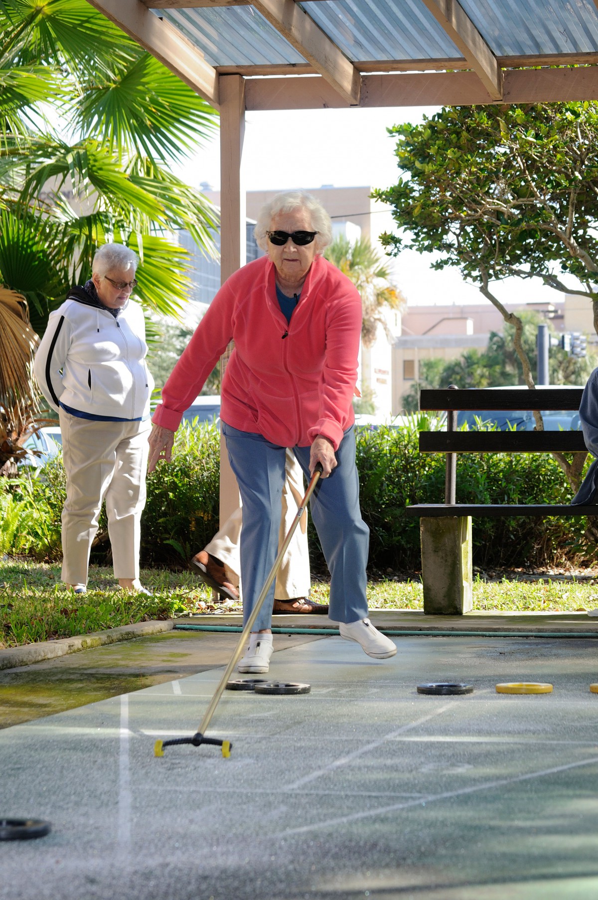 A senior woman enjoying a game of shuffleboard outdoors on a sunny day.