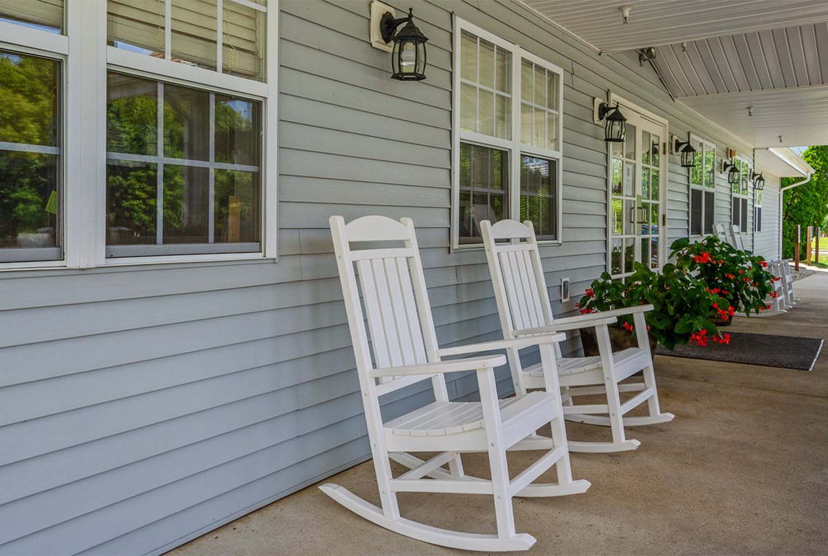 A cozy porch with two white rocking chairs and windows along the house exterior.