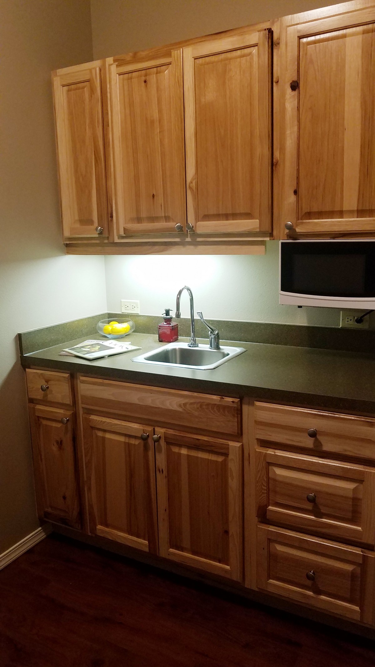 A small kitchen area with wooden cabinets and a countertop featuring a sink and microwave.