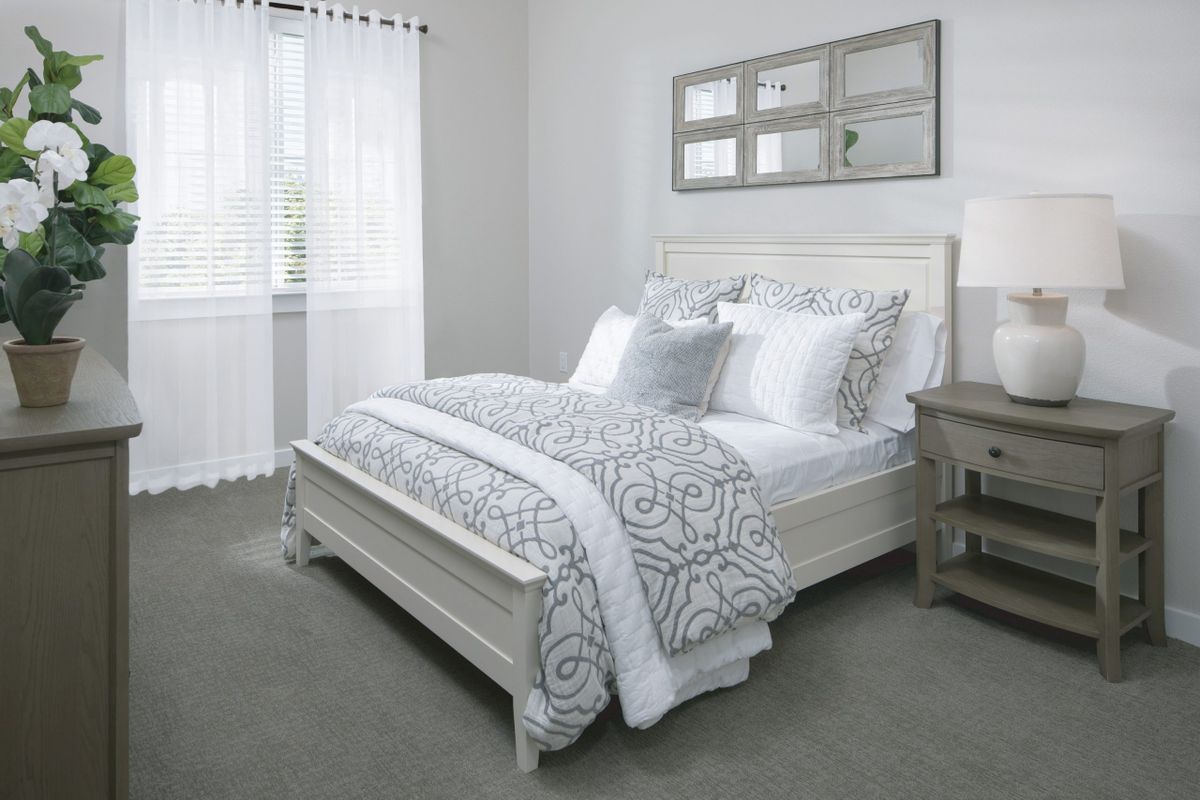 A neatly arranged bedroom featuring a bed with patterned bedding, a nightstand, and natural lighting from the window.