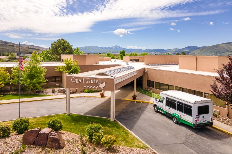 A hospital entrance with a bus parked in front, surrounded by mountains and a clear sky.