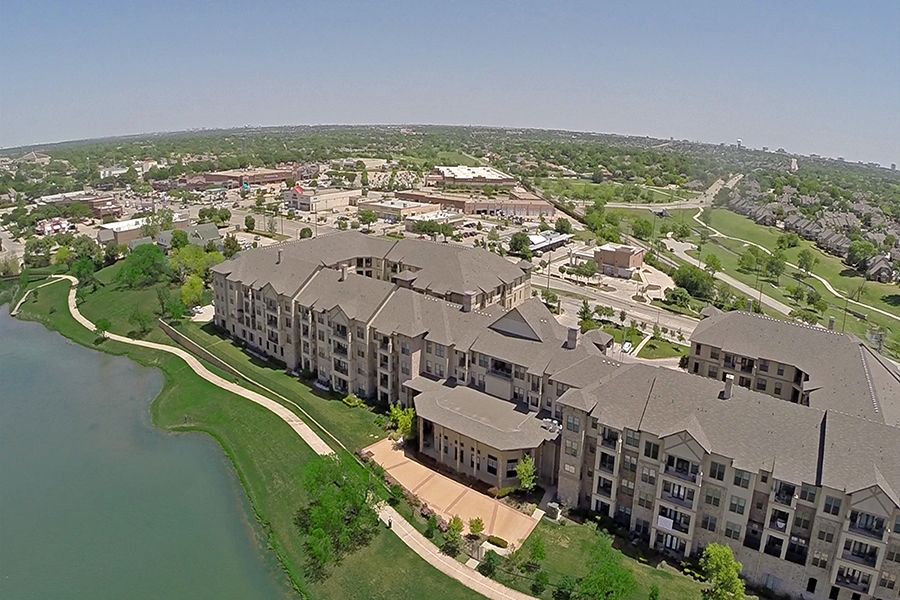 Aerial view of a residential apartment complex with a nearby lake and surrounding greenery.