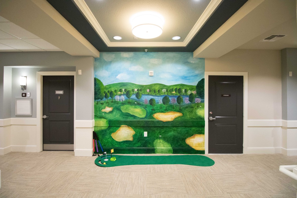 An indoor putting green setup in a hallway, featuring a golf-themed wall mural.